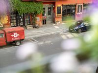 a red delivery truck is parked outside of a restaurant near the street with flowers growing out of the window