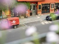 a red delivery truck is parked outside of a restaurant near the street with flowers growing out of the window