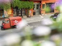 a red delivery truck is parked outside of a restaurant near the street with flowers growing out of the window