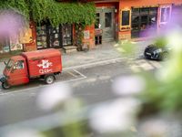 a red delivery truck is parked outside of a restaurant near the street with flowers growing out of the window