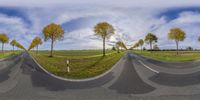 a panoramic photo of road through the field with trees and sky in the background