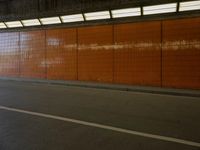 a person riding an orange skateboard on a road next to a wall with a light