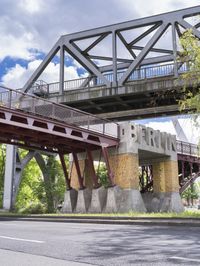 an old rusted train bridge and a paved street under a cloudy blue sky above