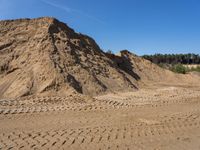 sand piles and a pile of dirt next to a forest under blue skies with trees