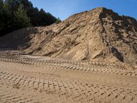 sand piles and a pile of dirt next to a forest under blue skies with trees