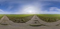 the 360 - lens view of a road with a grass field in the background and clouds overhead