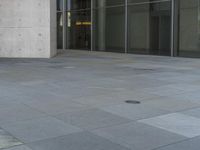 a man rides his skateboard down an empty sidewalk with tall glass walls behind him