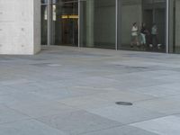 a man rides his skateboard down an empty sidewalk with tall glass walls behind him