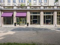 a group of people stand outside a store front with purple awnings and trees