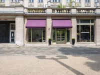 a group of people stand outside a store front with purple awnings and trees