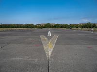 a yellow arrow pointing up to an upward point on a runway at an airfield with houses in the background