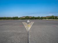 a yellow arrow pointing up to an upward point on a runway at an airfield with houses in the background