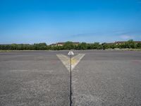 a yellow arrow pointing up to an upward point on a runway at an airfield with houses in the background