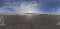 a fisheye lens view of an asphalt road with a sun and blue sky in the background