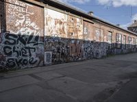 graffiti adorns a brick wall in an industrial area with a sidewalk in front of it