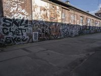 graffiti adorns a brick wall in an industrial area with a sidewalk in front of it