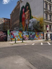 a wall with different colorful artwork on it in a city with buildings around and the street has a bike path going under it