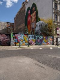 a wall with different colorful artwork on it in a city with buildings around and the street has a bike path going under it