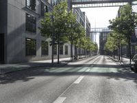 a empty street lined with trees and buildings in a city with a pedestrian bridge above the buildings