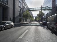 a empty street lined with trees and buildings in a city with a pedestrian bridge above the buildings