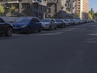 a street lined with parked cars in front of apartment blocks on a sunny day on the sidewalk