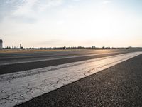 a paved runway with white paint and grass behind it and water tower at the end of the road