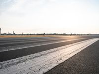 a paved runway with white paint and grass behind it and water tower at the end of the road