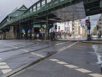 a bridge with people standing under it and a train crossing it over tracks in the street