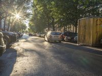 the sun shines on parked cars along a tree lined street in an urban setting