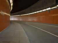 a long dark tunnel with orange bricks and a man on a skateboard riding down one of the walls