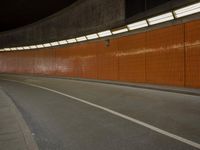 a long dark tunnel with orange bricks and a man on a skateboard riding down one of the walls