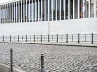 a person walks by some kind of street side building by a fence and brick road