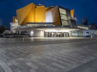 a lighted building with a bunch of people outside at night time and lights on the floor