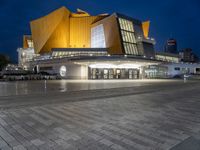 a lighted building with a bunch of people outside at night time and lights on the floor