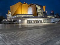 a lighted building with a bunch of people outside at night time and lights on the floor