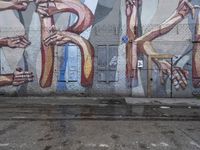 graffiti adorns the side of an old factory with graffiti letters and hands and feet