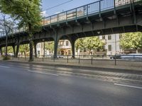 a road with parked cars is shown under an overpass on the bridge on which there are cars that are driving down the street