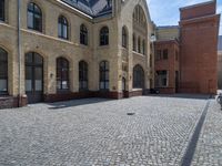 the sidewalk is paved with stones and has a bench in front of it, with no people inside