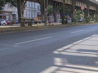 a person riding on a bike down the middle of a road next to a train bridge