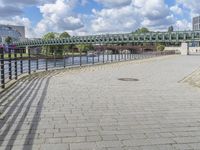 a path along the river with metal railings and buildings along it below the water