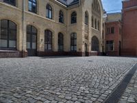 the sidewalk is paved with stones and has a bench in front of it, with no people inside