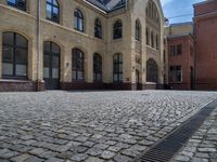 the sidewalk is paved with stones and has a bench in front of it, with no people inside