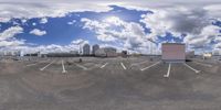 an empty parking lot on a partly cloudy day with a sky background and buildings behind it