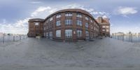 the circular shot shows a view of an area from a skate park near a large brick building