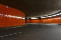 the tunnel under the highway at night has an orange wall and flooring with light