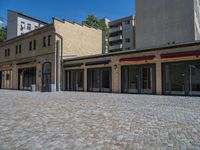 the sidewalk is paved with stones and has a bench in front of it, with no people inside