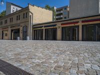 the sidewalk is paved with stones and has a bench in front of it, with no people inside