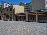 the sidewalk is paved with stones and has a bench in front of it, with no people inside