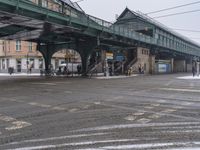 a green pedestrian bridge and cars passing under it on a snowy day, with a sidewalk in the foreground