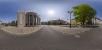 this 360 - vision lens image of an empty street shows a building and trees with a lightpost